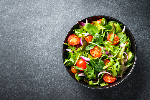 Salad in black bowl at dark background. Healthy green vegetable salad, diet menu. Top view.