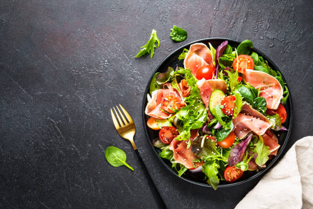 Fresh salad with jamon, green salad leaves and tomatoes.