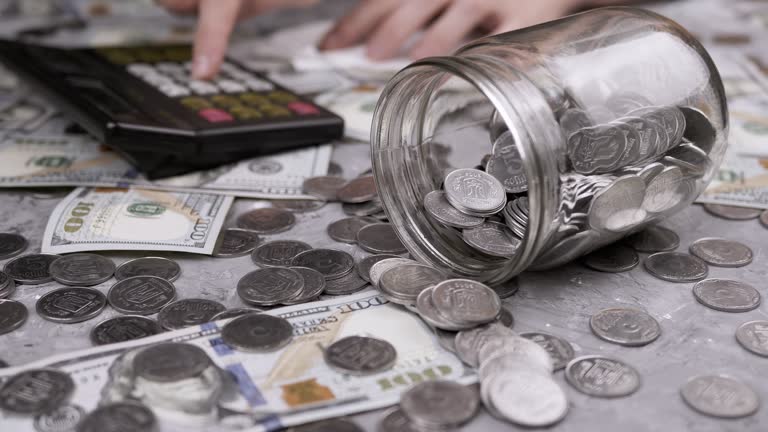 Woman Counting Expenses on a Calculator on Paper in Front of a Jar with Coins. 4K