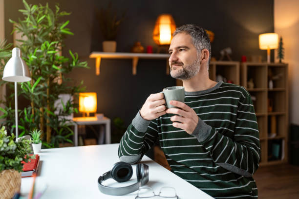 istock Relaxed mid-adult Caucasian man looking through window while having a coffee 1987546436