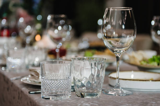 istock Serving, setting table in a restaurant. Plate and glass, stack, wineglass, luxury rich decor. Wedding set up, dinner table reception. Birthday, baptism, event. Closeup details of interior. 1987560699