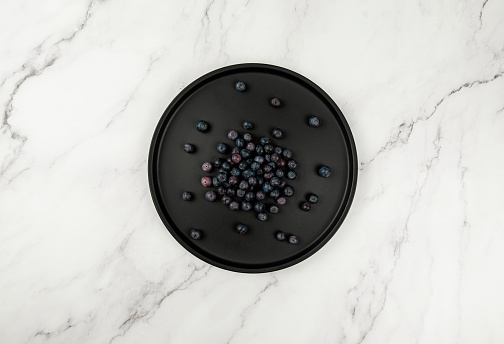 Top view of black plate on white marble background. Blueberries flat lay. Copy space.