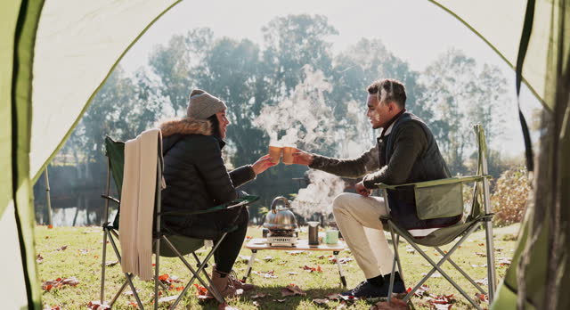 Coffee cup, tent and couple of friends toast, bond and camping in nature countryside, woods and forest field. Wellness, camper freedom and people cheers with hot chocolate, tea and drinks in campsite