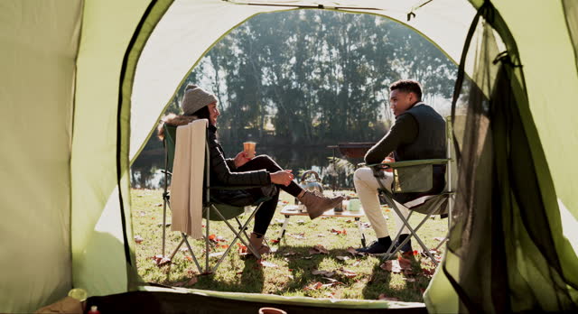 Couple, camping and back with tent, coffee or relax in morning on adventure, vacation or outdoor by lake. Man, woman and conversation for holiday together, freedom and chair on lawn, woods or forest