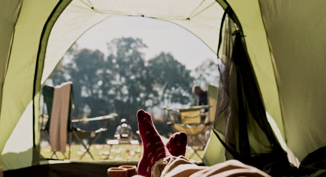 Nature, camping tent and feet of person relax, rest and enjoy freedom, natural stress relief or morning air in outdoor forest. Wellness, socks and legs of camper on park campsite, holiday or vacation