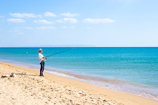 A fisherman in a hat catches fish with a fishing rod in the Black Sea on a summer day. Pastime for retirees.09.17.2023 Anapa, Russia