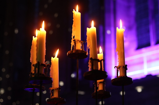 Candles burning in a traditional metal candlestick holder, inside a church at night