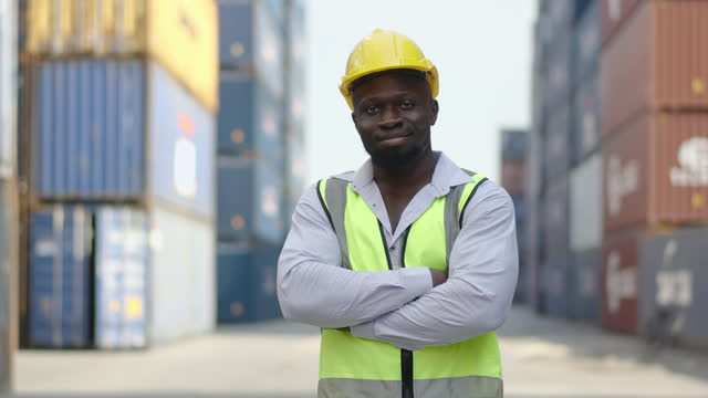 Portrait of african american container male worker or dock foreman confident and smiling standing at warehouse logistic in Cargo freight ship for import export in harbor, happy employee arms crossed