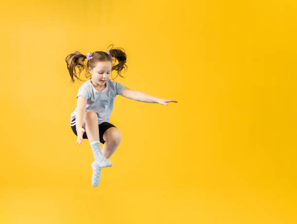 istock Happy little girl jumping on yellow background 1987608642