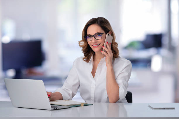 istock Mid aged businesswoman using laptop and smartphone at the office 1987609193
