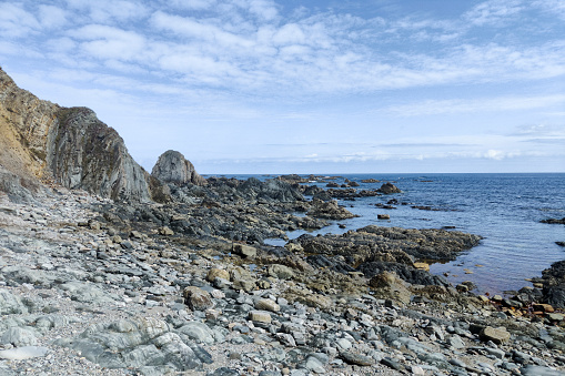 serene coastal landscape with large, rugged rocks extending into calm ocean waters under a partly cloudy sky