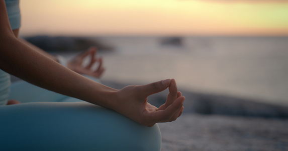 Person, hands and meditation on beach in sunset for spiritual wellness, inner peace or outdoor zen. Closeup of yogi in meditate, exercise or yoga for health, awareness or chakra by the ocean coast