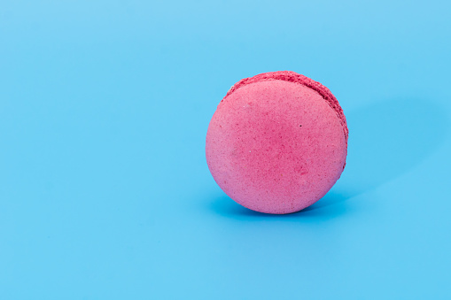 Pink french macaroon or macaron on blue background. Tasty colorful macarons. Cookie made of two smooth halves, fastened with stringy fillings. French pastry made from egg whites.