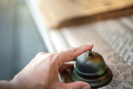 A guest's hand is ringing bell which is placed on the counter desk for calling the restaurant waiter. Action for business concept scene. Close-up and selective focus.