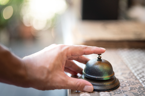 A guest's hand is ringing bell which is placed on the counter desk for calling the restaurant waiter. Action for business concept scene. Close-up and selective focus.