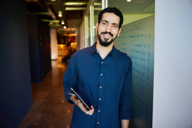 istock Smiling businessman with a tablet leaning on a wall in an office 1987631972