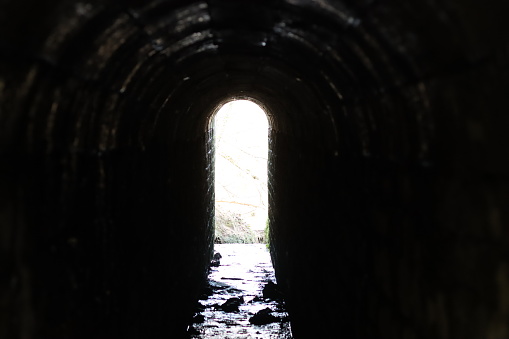 View through an arched tunnel carrying a stream beneath a bridge