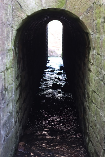 View through an arched tunnel carrying a stream beneath a bridge
