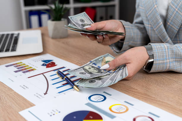 istock close up woman holding dollars working at office with business graph and chart 1987653254