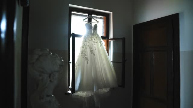Wedding dress hanging of the window in the room.
