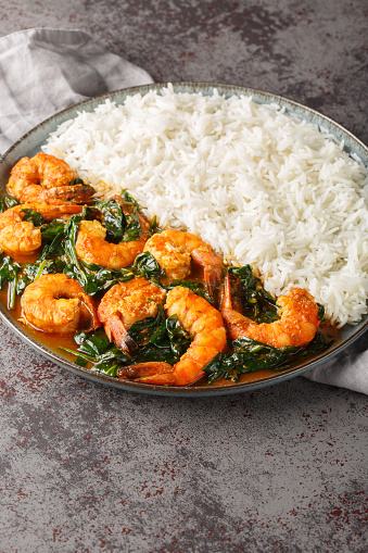 Shrimp Saag is an flavorful curry made with juicy prawn, onion, garlic, ginger, spinach and aromatic spices served with rice closeup on the plate on the table. Vertical