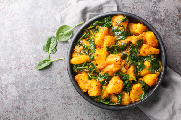 Saag aloo is a classic Indian style side dish featuring potatoes fried in spices and spinach closeup on the bowl. Horizontal top view