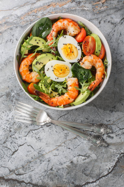 istock Mediterranean shrimp salad with avocado, arugula, spinach, tomatoes and boiled eggs close-up in a bowl. Vertical top view 1987661076