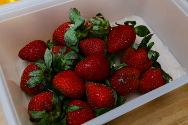 istock strawberries in a plastic container on a wooden table 1987663731