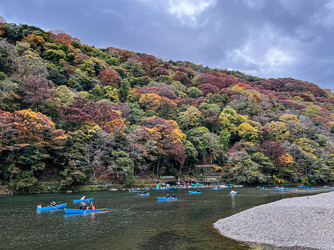 The lake in the Japanese mountains. Hills are covered with coloured autumn leaves. People are sailing in small boats. Perfect relaxation.