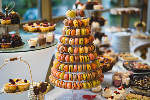 Delicious wedding reception candy bar dessert table with various macarons, sweets, cupcakes, fruits and pies.