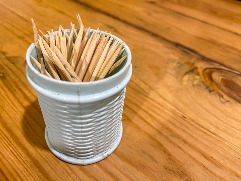 A toothpick is a small thin stick of wood, plastic, bamboo, metal, bone to remove detritus from teeth. Tube full of toothpicks on wooden table with empty blank text copy space.