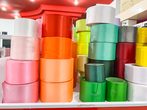 Rolls of colorful ribbons stacked on a display shelf in a knick-knack shop. Wide plastic ribbon tape is Materials for making crafts and art