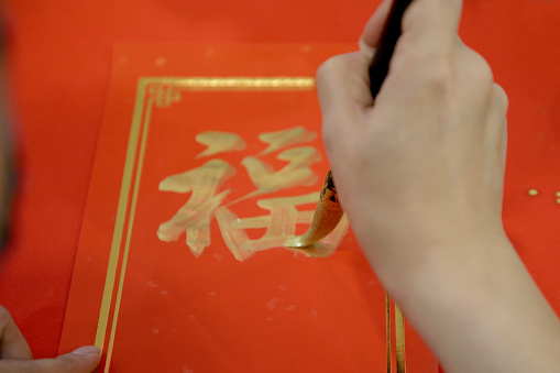 A man's hand is writing Chinese calligraphy on a piece of red paper for Chinese New Year greetings