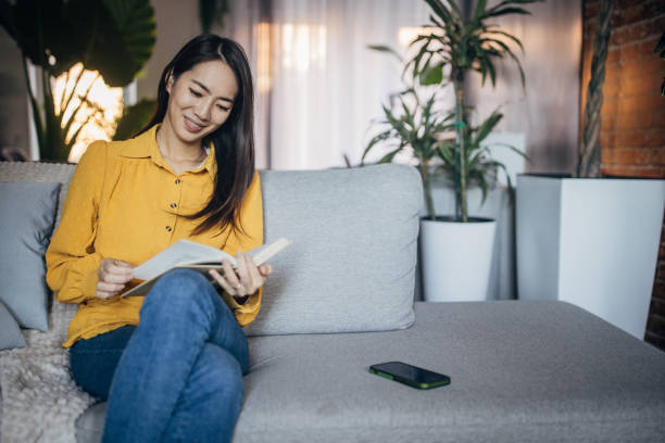 istock Young Japanese woman reading book at home 1987736639
