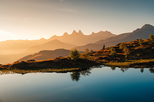 Picturesque landscape of golden sunrise over Arves massif with lonely tree relfection on Lac Guichard at French Alps, France