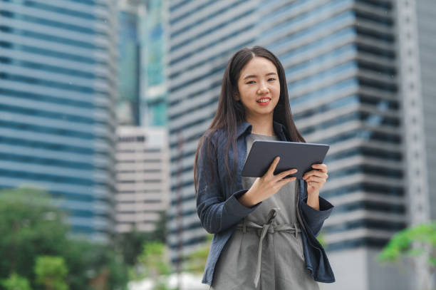 istock Tech-Infused Tranquility: Young Asian Woman Navigating the Urban Landscape with her Tablet 1987753376