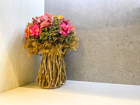 Plastic artificial bunch of dried flower bouquet in vase on the table. Modern interior design of modern office work room or workplace with artificial plant. Imitation flowers.