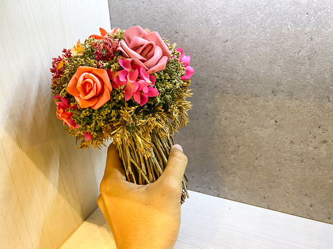 Someone hand holding plastic artificial bunch of dried flower bouquet for girlfriend gift. Imitation flowers. Empty blank copy text space.