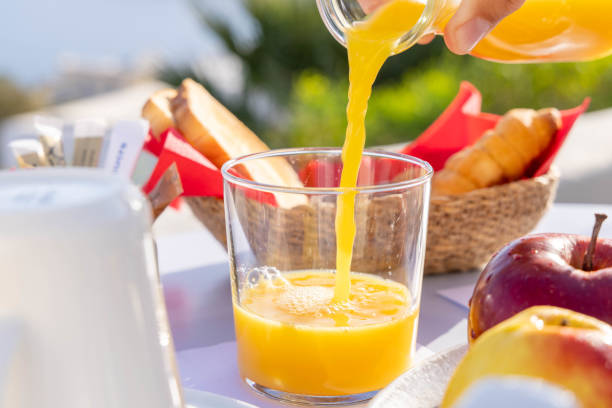 istock Citrus Elegance: Hand-Poured Fresh Orange Juice on Breakfast Table with Greek Landscape as Backdrop 1987766158