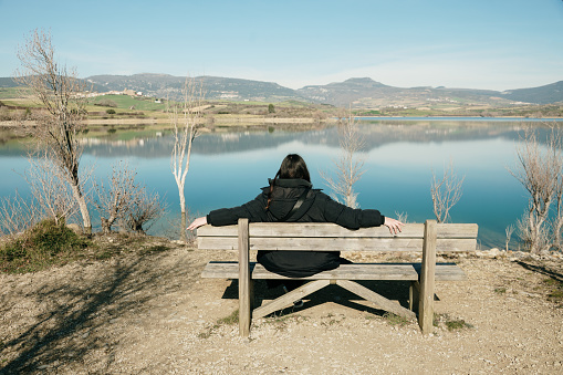 Rear view of a woman sitting on a bench and contemplating a beautiful lake