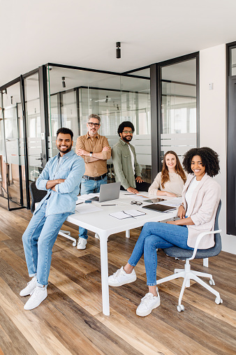 A vibrant team gathers around a minimalist white table in their bright office, embodying the energy and collaboration of a modern, dynamic workplace, diverse ages and ethnic collaborate together