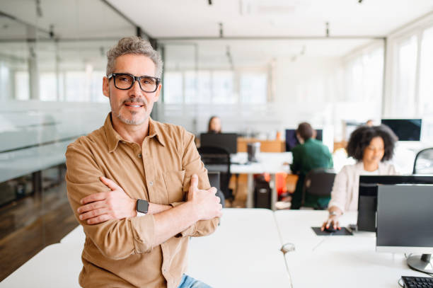 istock Senior professional is leaning an office desk, confidently overseeing the workspace 1987789348