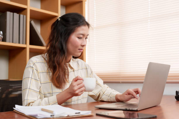 istock Contemplative Asian office worker holds coffee mug, pausing thoughtfully amidst her busy work schedule. Warmth and thought intersect as this Asian professional takes reflective coffee break in office 1987792537