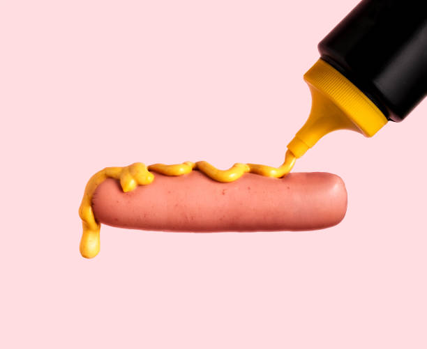istock Pouring mustard on hot sausage on pink background 1987802786
