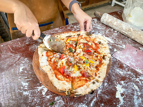 A woman wearing apron is slicing a pizza into pieces to serve during an italian pizza cooking class session