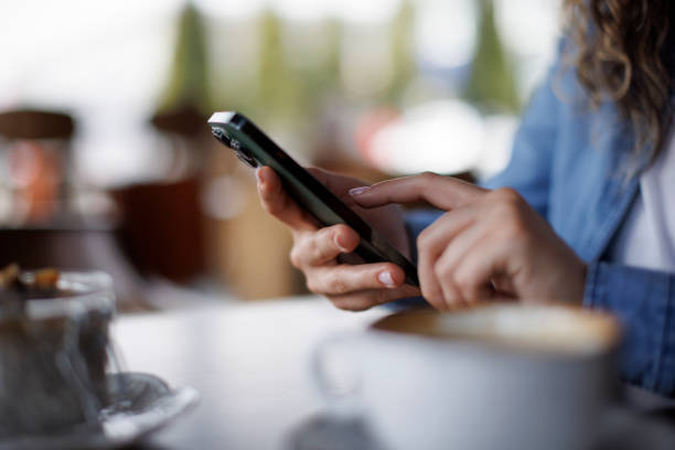 istock Closeup hands of woman while using mobile phone and drink coffee at cafe 1987830380