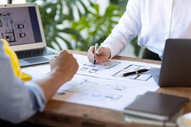 istock Brainstorming group of architects and engineers discuss building blueprint design on laptop and construction project planning on wooden table in office. 1987834154