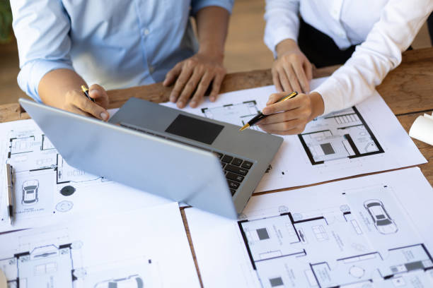 istock Brainstorming group of architects and engineers discuss building blueprint design on laptop and construction project planning on wooden table in office. 1987834692
