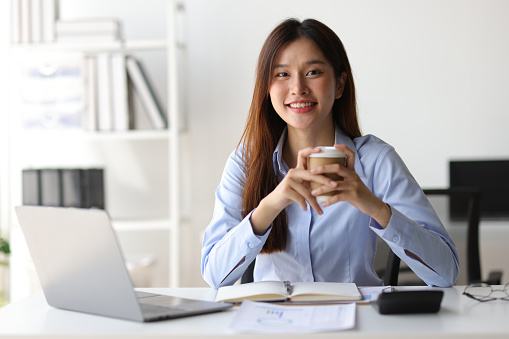 Portrait of a charming Asian businesswoman in casual clothes drinking hot coffee and relaxing during a break in the office.