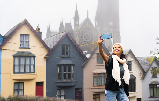 Smiling woman taking a selfie in a small town in Ireland known for its colorful houses and cathedral on a foggy day